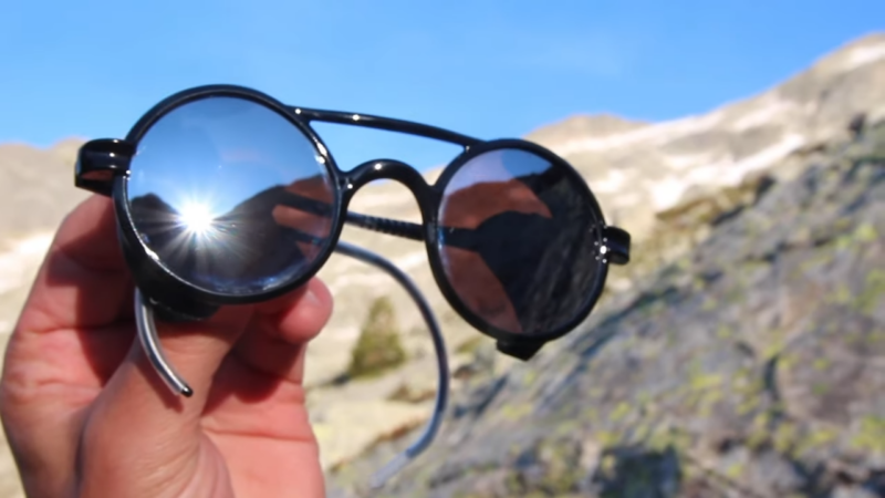 Black Sunglasses with Reflective Lenses Held in The Mountains