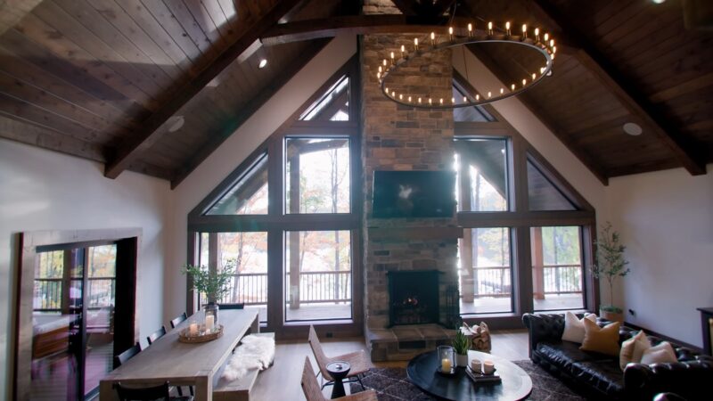 A spacious cabin living room featuring high vaulted wooden ceilings, a stone fireplace, large windows