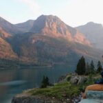 A Person Sitting by A Lake, Enjoying the Scenic View of The Mountains in Glacier National Park